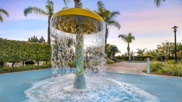 A water feature with a yellow dome and a striped pole, surrounded by a pool and palm trees.