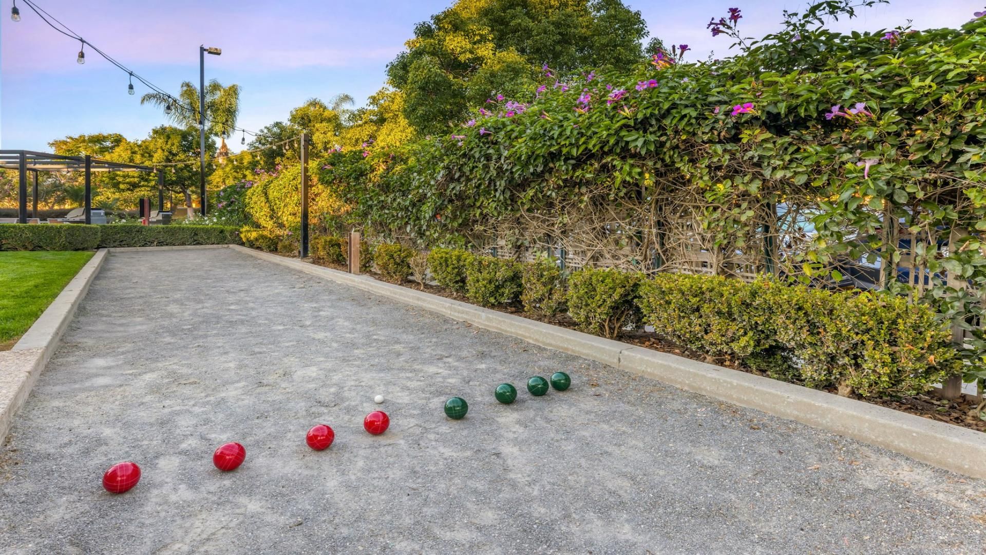 A courtyard with a shuffleboard court, surrounded by greenery and a pergola.