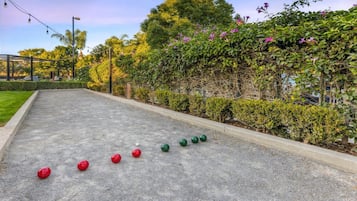 Un patio con una cancha de shuffleboard, rodeado de follaje y una pérgola.