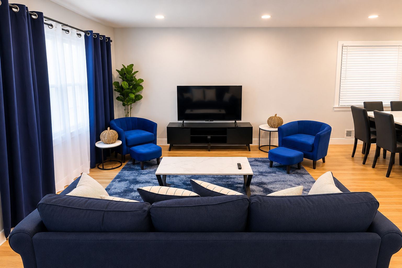 A modern living room with a sofa, two armchairs, a coffee table, a TV, and a dining area with chairs and a table.