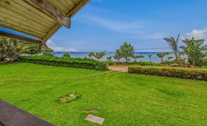 A well-maintained lawn with a pathway leading to a beach, under a wooden structure.
