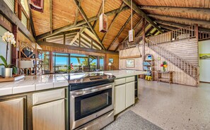 A spacious kitchen with a large island, a wooden staircase, and a view of the outdoors.