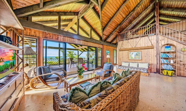 A spacious living area with a high ceiling, large windows, and a view of the outdoors.
