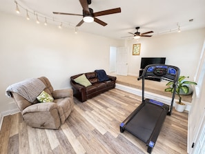 A living room with a treadmill, a brown leather sofa, a recliner, and a ceiling fan.