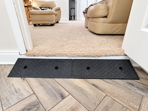 A room with a beige carpet, a black mat at the entrance, and a wooden floor.