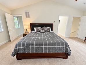 A bedroom with a large bed, a nightstand, a lamp, and a window.