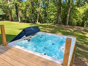 A hot tub with a wooden deck, surrounded by a grassy area and trees.