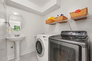 Een kleine wasruimte met een wasmachine, een spoelbak en twee rieten manden op een plank.
