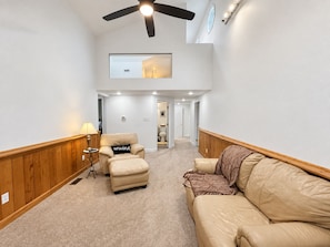 A spacious living area with a high ceiling fan, a leather sofa, a recliner, and a lamp.