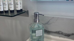 Un lavabo de salle de bain avec un distributeur de savon liquide et une étagère contenant plusieurs flacons de produits de toilette.