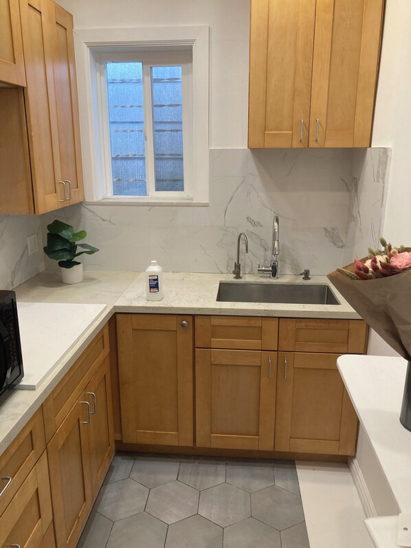 A kitchen with wooden cabinets, a marble backsplash, a window, and a sink.