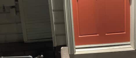 A red door with a white frame, a small step leading up to the entrance, and a utility meter box on the ground.