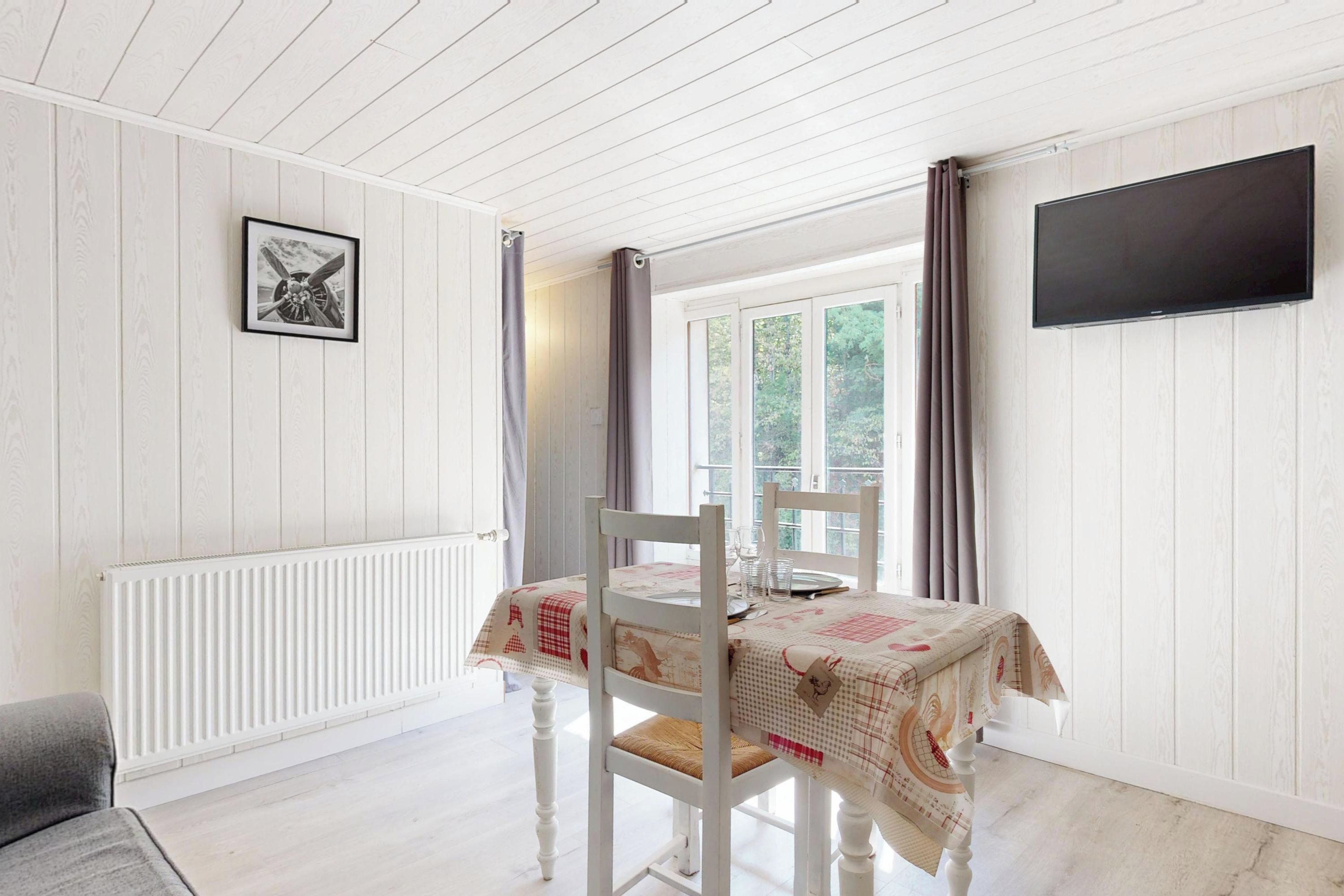 A room with a dining table set for two, a radiator, a framed picture on the wall, and a TV mounted on the wall.