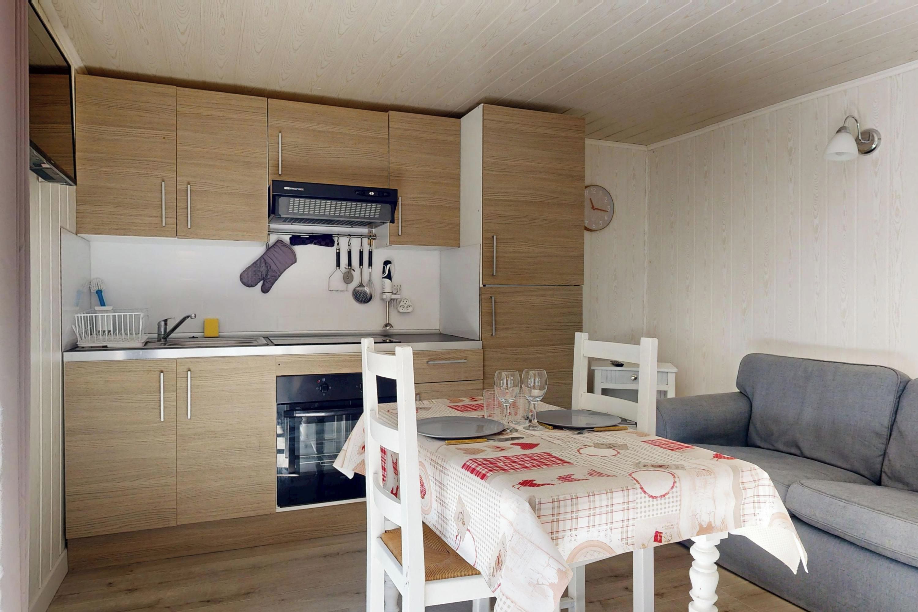 Cocina compacta con armarios de madera, microondas integrado y comedor con mesa lista para dos personas.