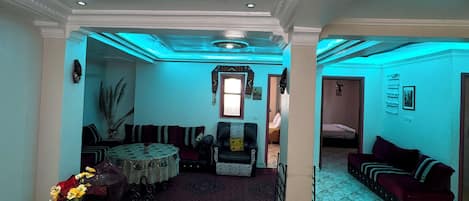 A room with a dining table, a sofa, a patterned rug, and a decorative ceiling.