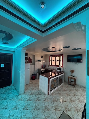 A kitchen with a marble floor, a central island, and a TV mounted on the wall. - Welcoming 2-bedroom apartment in vibrant Aourir perfect for relaxing stay (Agadir)