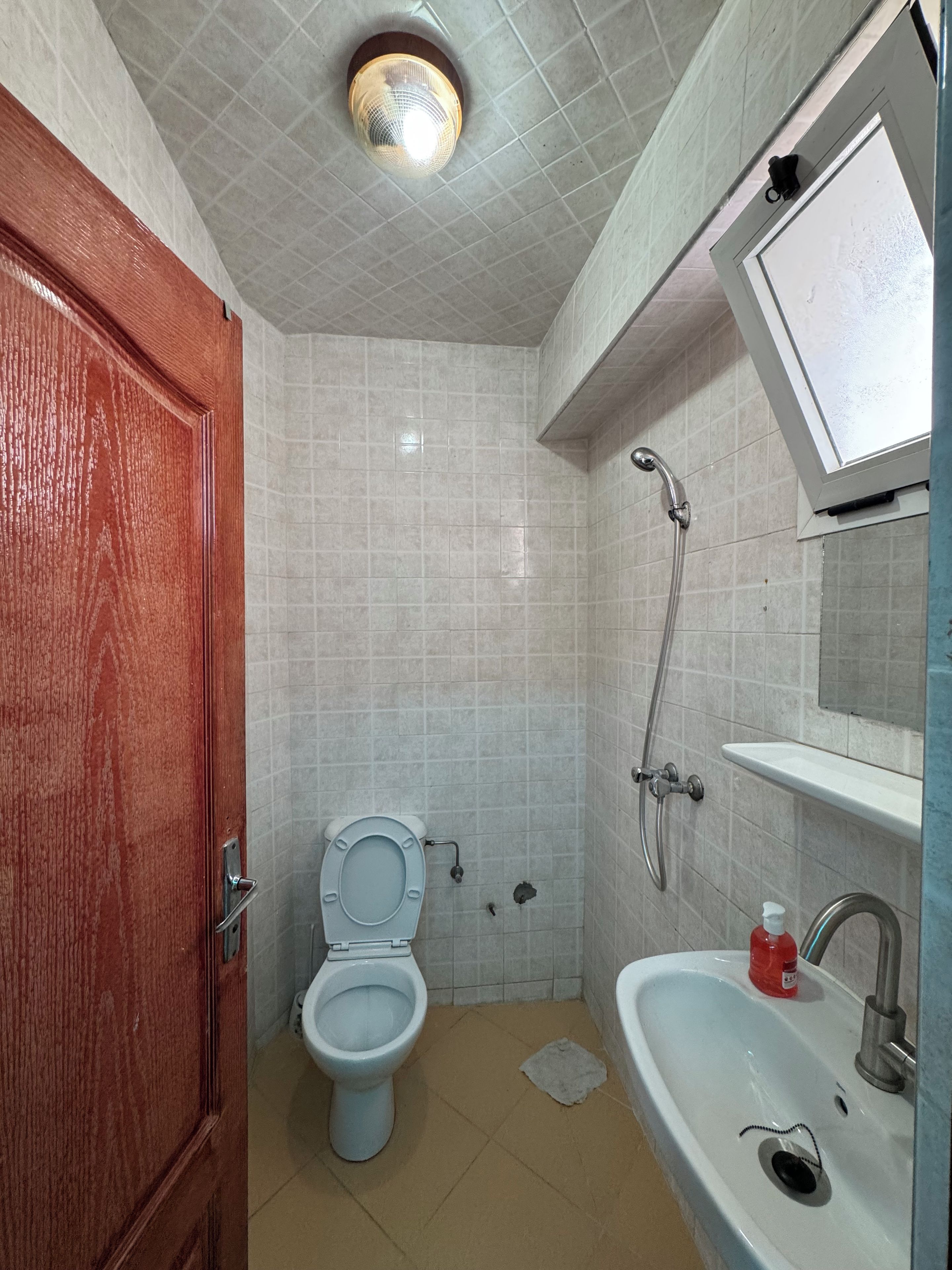 Un baño con inodoro, lavamanos, ducha y una lámpara en el techo.