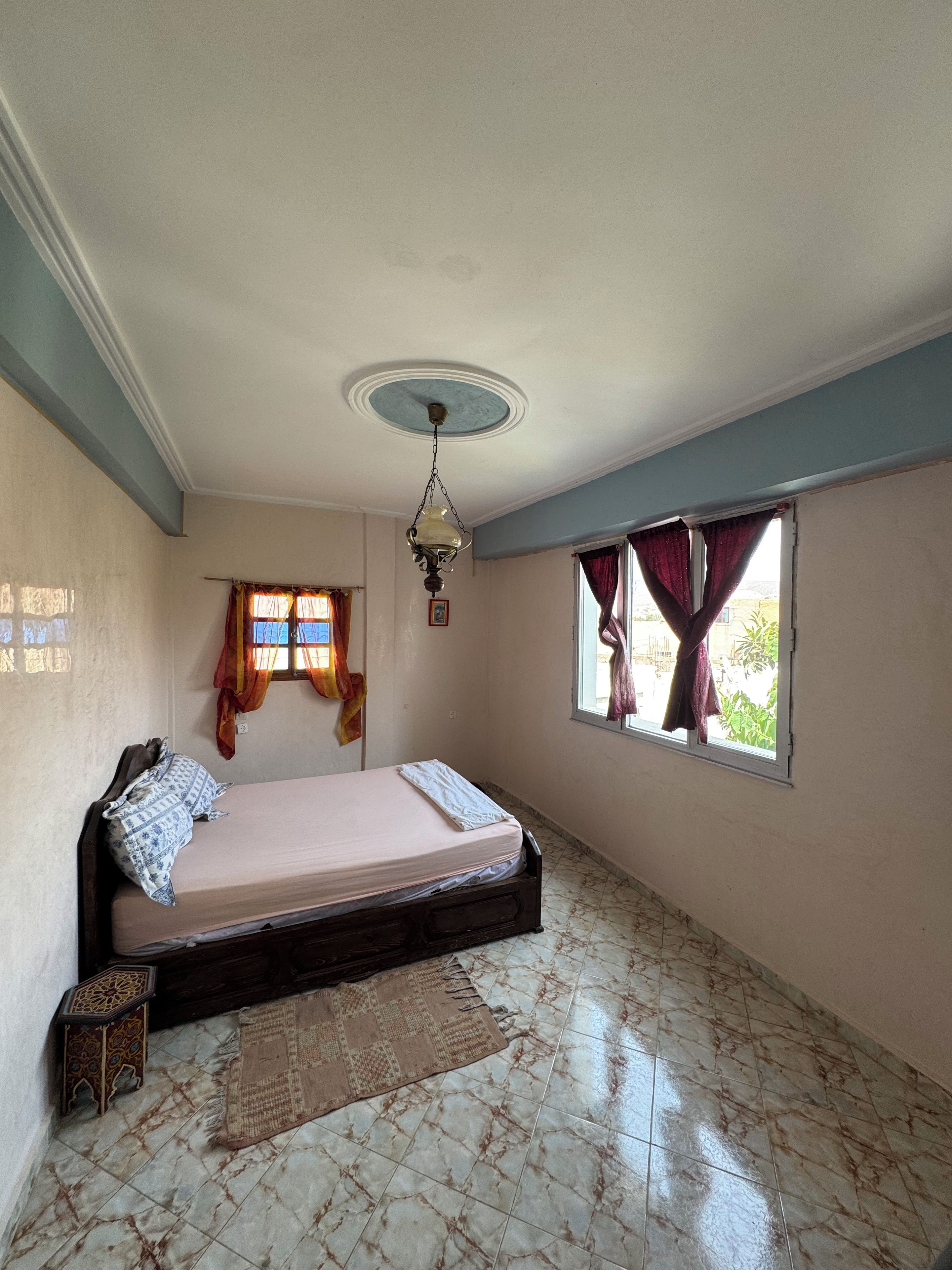 A room with a bed, a window with curtains, a ceiling fan, and a patterned rug.