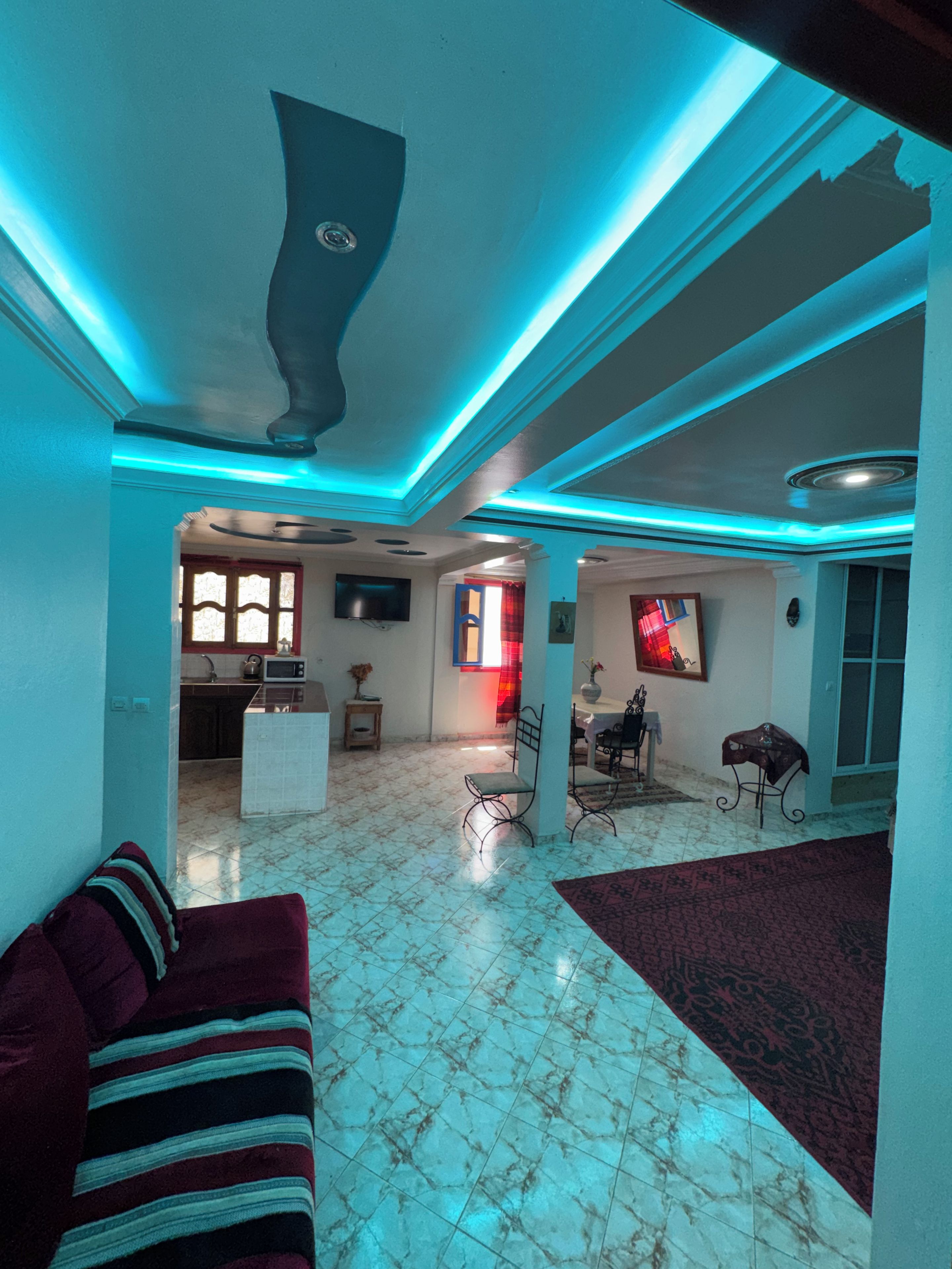 A spacious living area with a tiled floor, a sofa, a dining table with chairs, and a kitchen in the background.