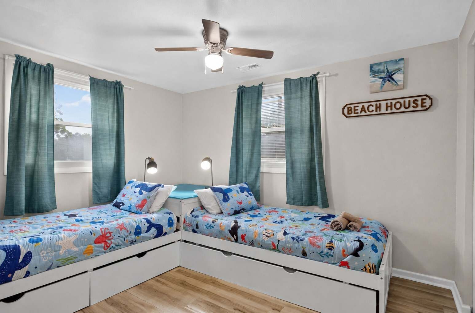 A bedroom with two beds, a ceiling fan, and a 'Beach House' sign.