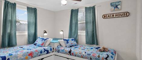 A bedroom with two beds, a ceiling fan, and a 'Beach House' sign.