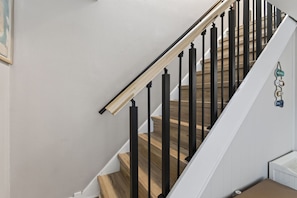 Eine Treppe mit Holzstufen und schwarzen Geländern, die zu einer Zwischenebene mit einer weißen Wand und einem kleinen dekorativen Gegenstand führt.