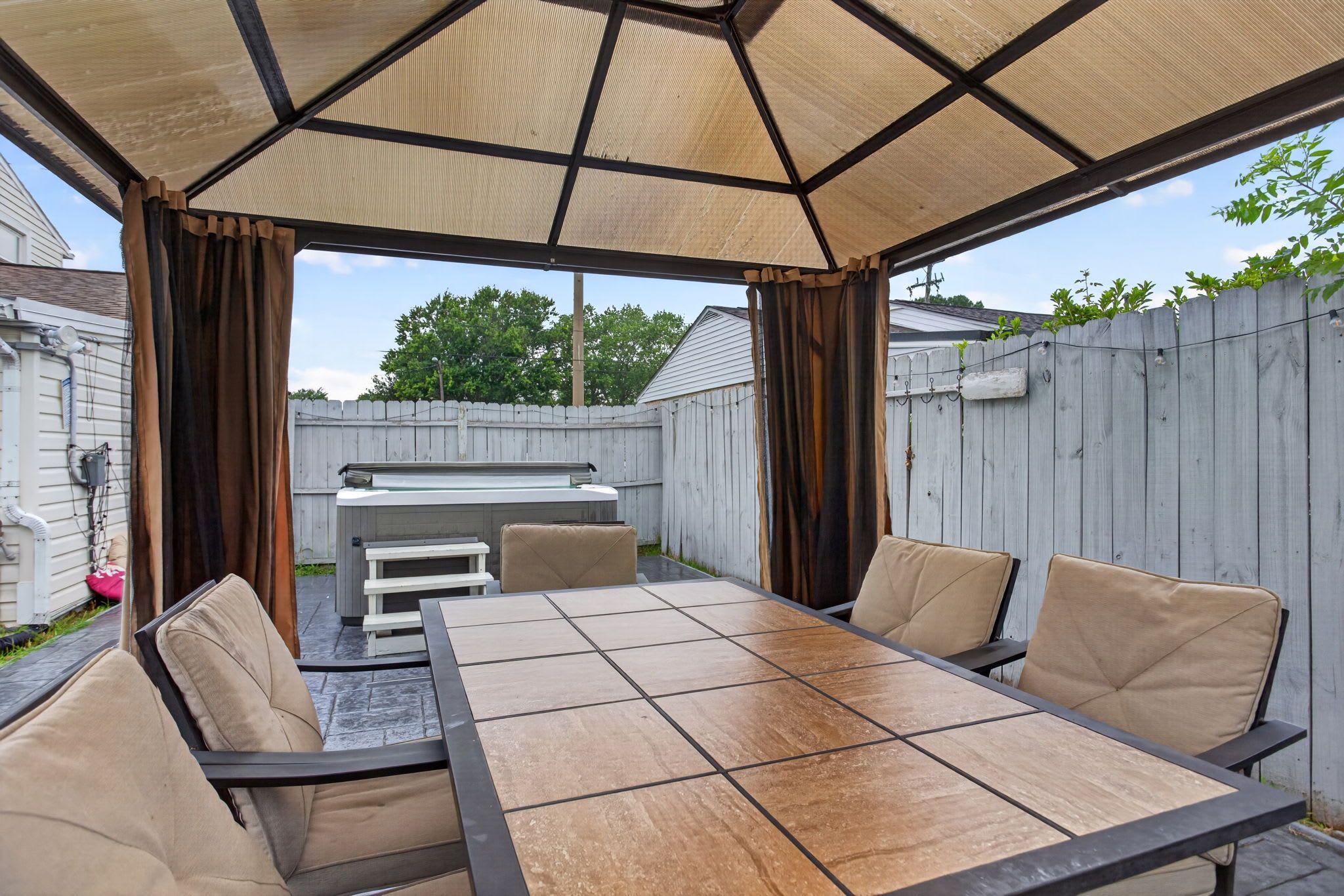 An outdoor patio with a table and chairs, a grill, and a covered area with curtains.