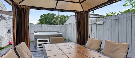 An outdoor patio with a table and chairs, a grill, and a covered area with curtains.