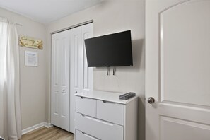Ein Zimmer mit einem weißen Kleiderschrank, einem Flachbildfernseher an der Wand und einer Tür mit einem runden Knauf.