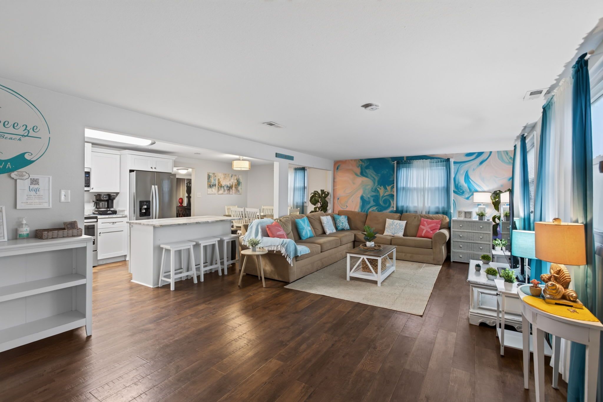 A modern living room with a sofa, coffee table, and a kitchen area with a refrigerator and bar stools.