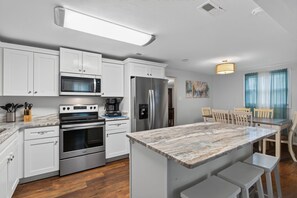 Eine moderne Küche mit weißen Schränken, Edelstahlgeräten, einer Kochinsel mit Marmorplatte und einem Essbereich mit Holzsesseln.