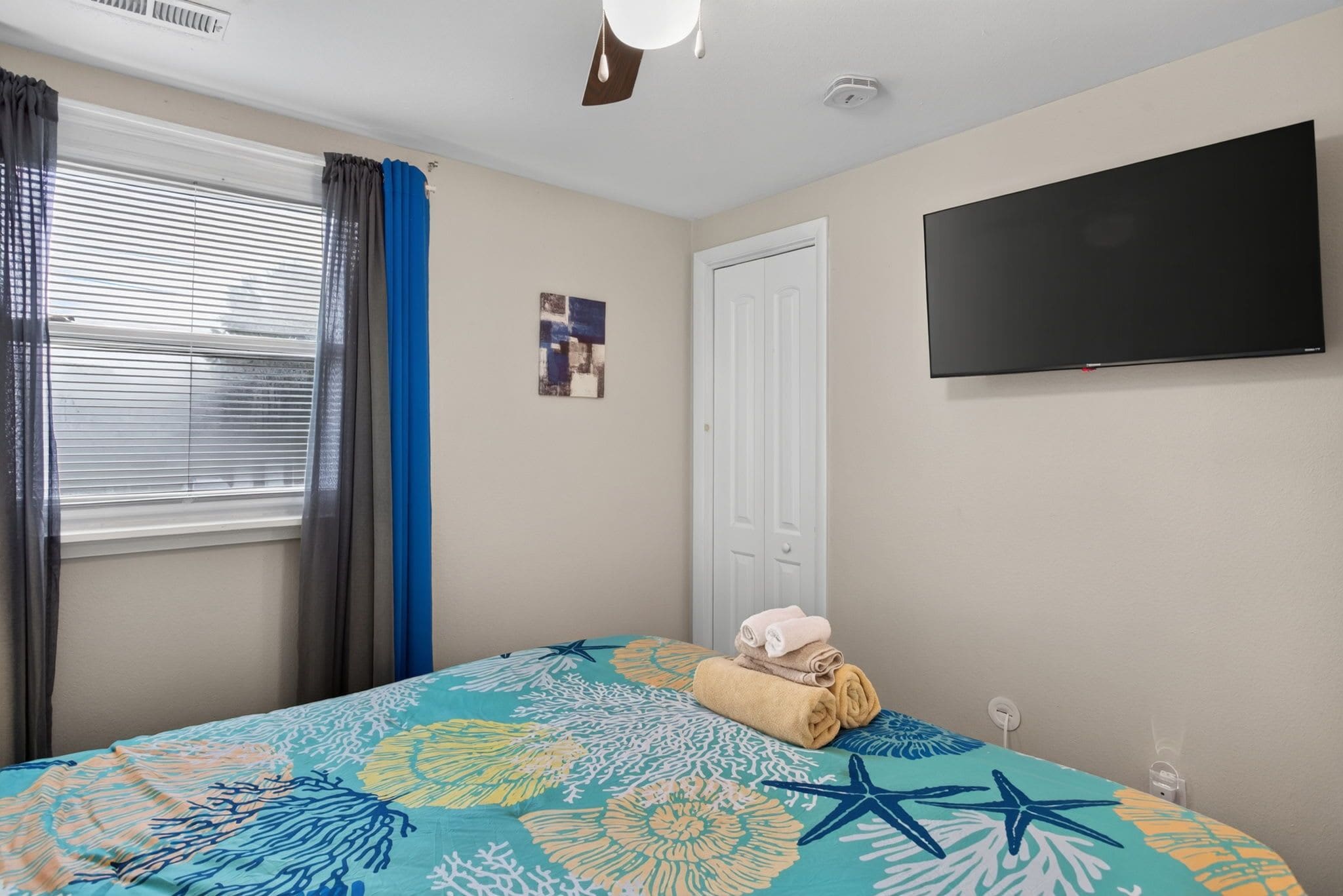 A bedroom with a bed, a flat-screen TV, a door, and a window with curtains.