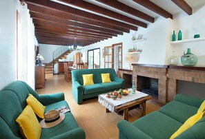 A living room with green sofas, a fireplace, and a dining area in the background. - Spacious Countryside Villa, A/C, Private Pool, Magnificent Views of s'Albufereta & Bay of Pollença! (Alcudia)