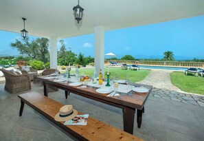 An outdoor dining area with a view of the sea, a pool, and lounge chairs. - Spacious Countryside Villa, A/C, Private Pool, Magnificent Views of s'Albufereta & Bay of Pollença! (Alcudia)