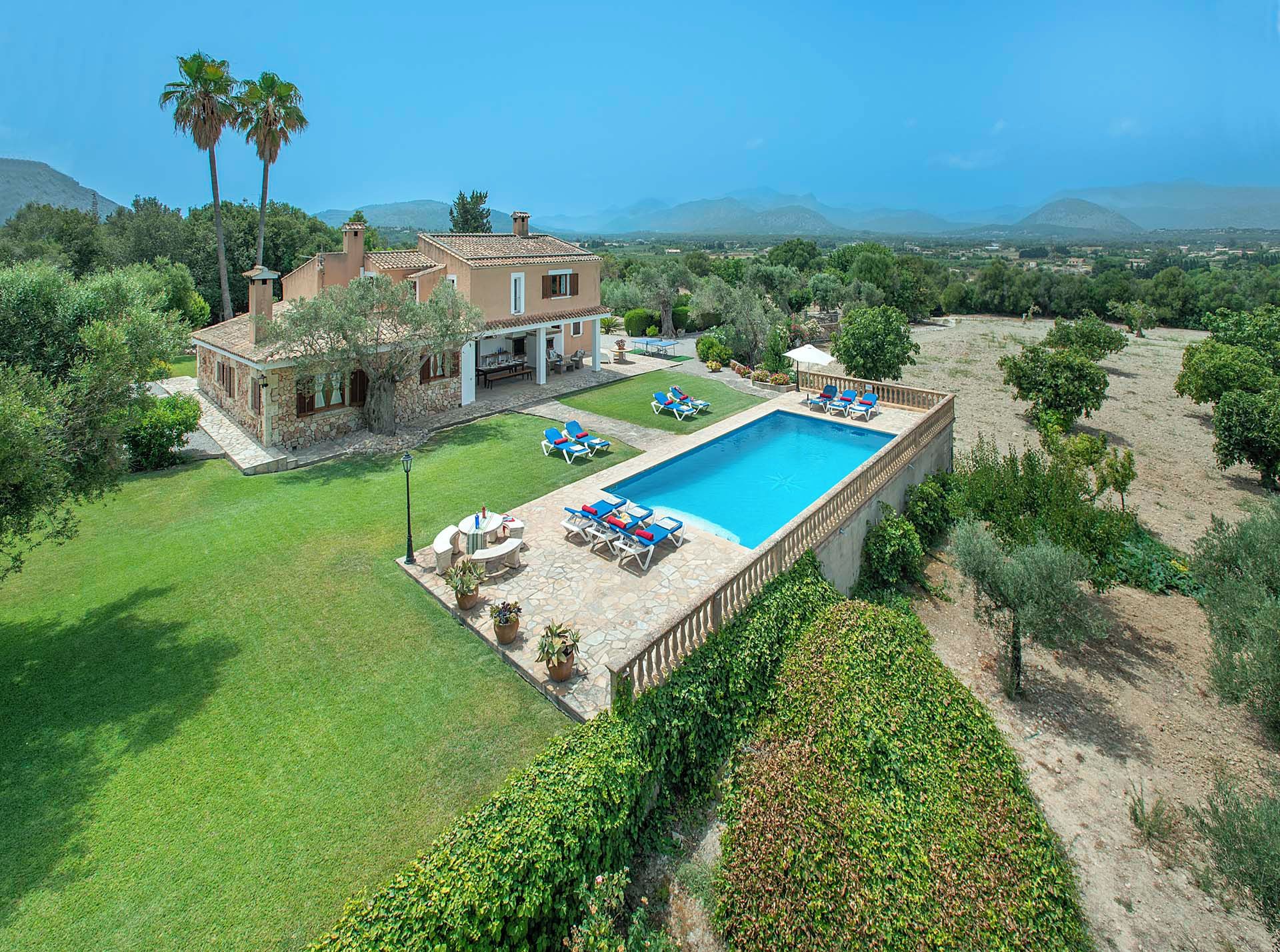 A large house with a swimming pool, surrounded by a well-maintained lawn and trees.