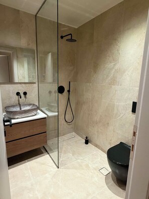 Une salle de bain moderne avec une douche à parois de verre, un lavabo avec un receveur en marbre et des toilettes aux couleurs sombres.