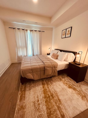 A bedroom with a bed, nightstands, a rug, and curtains. - Stylish 2 Bed, 2 Bath St. Catharines Retreat | Free Parking (St. Catharines)
