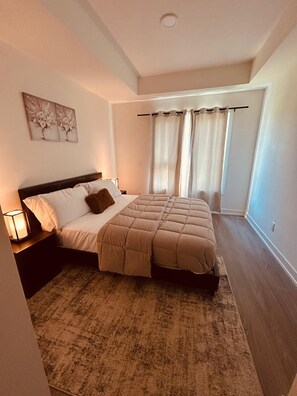 A bedroom with a bed, a nightstand, a lamp, a rug, and a window with curtains.