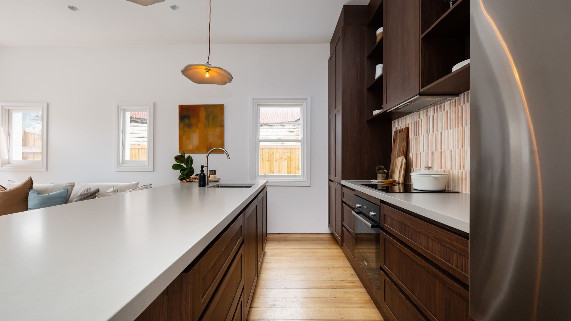 A modern kitchen with a large island, wooden cabinets, and a stainless steel refrigerator.