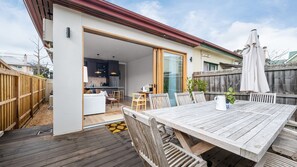 A wooden deck with a dining table and chairs, a sliding glass door leading to a modern kitchen, and a wooden fence. - Bellamy Richmond by Property Mums (Richmond)