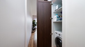 A laundry room with a washing machine, shelves with cleaning supplies, and a potted plant. - Bellamy Richmond by Property Mums (Richmond)