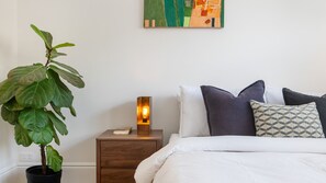 A bedroom with a bed, pillows, a bedside table with a lamp, and a potted plant. - Bellamy Richmond by Property Mums (Richmond)