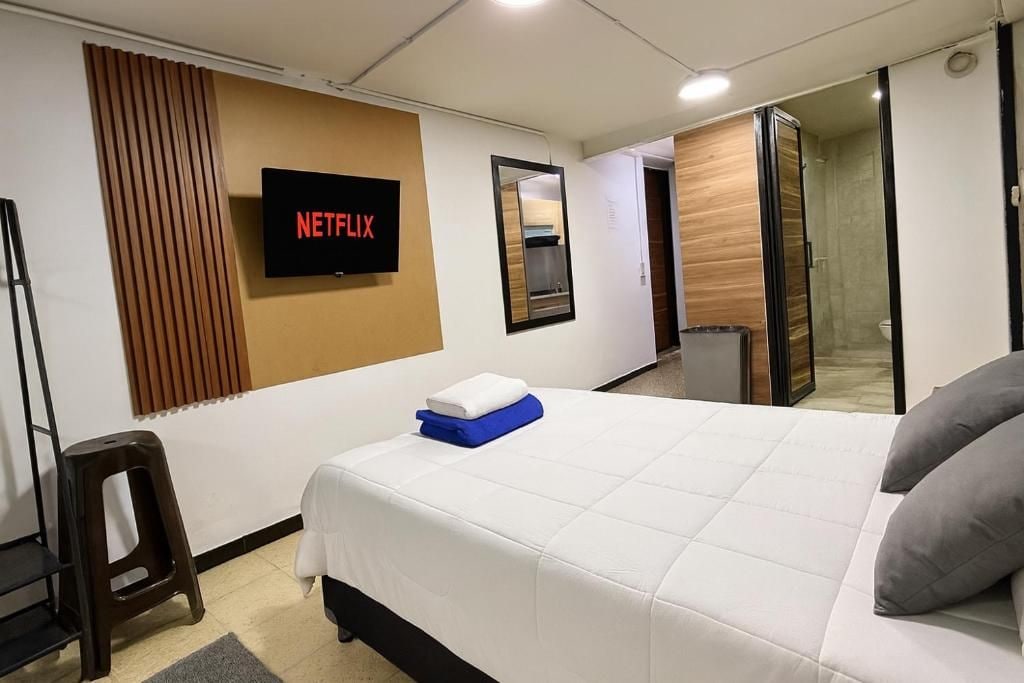 Habitación de hotel con cama, televisor montado en la pared, espejo y puerta que da a un baño.