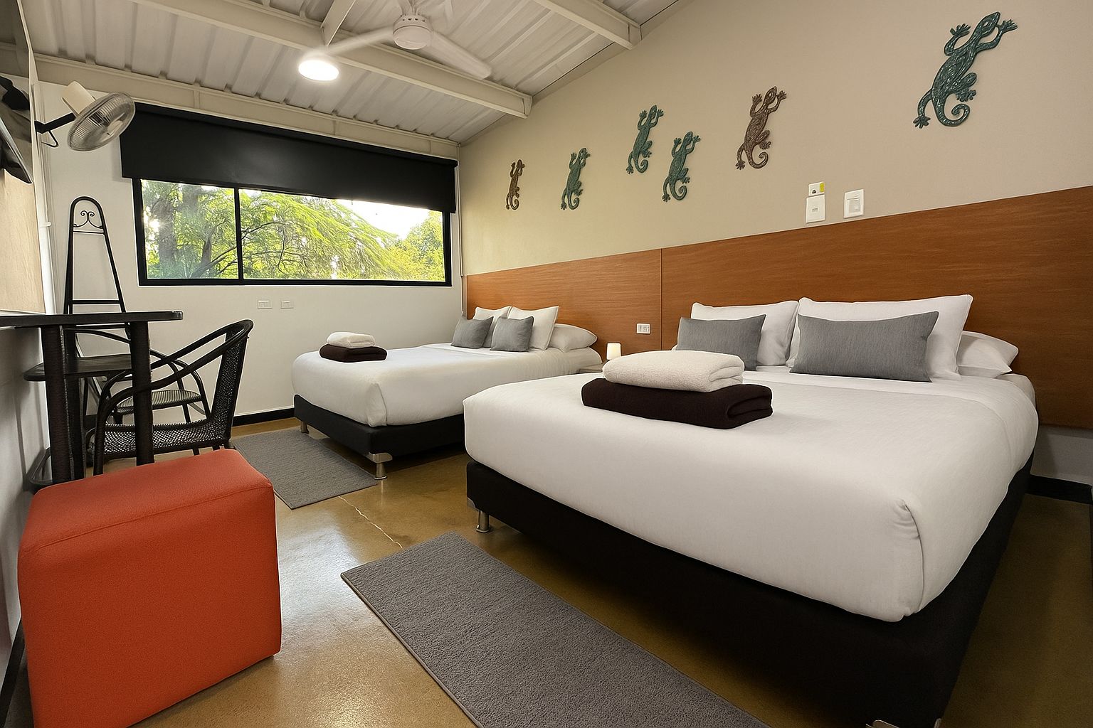 Habitación de hotel con dos camas, un escritorio, una silla y ventana con vista a árboles.