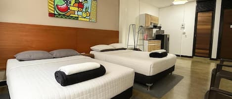 A hotel room with two beds, a kitchenette, and a painting on the wall.