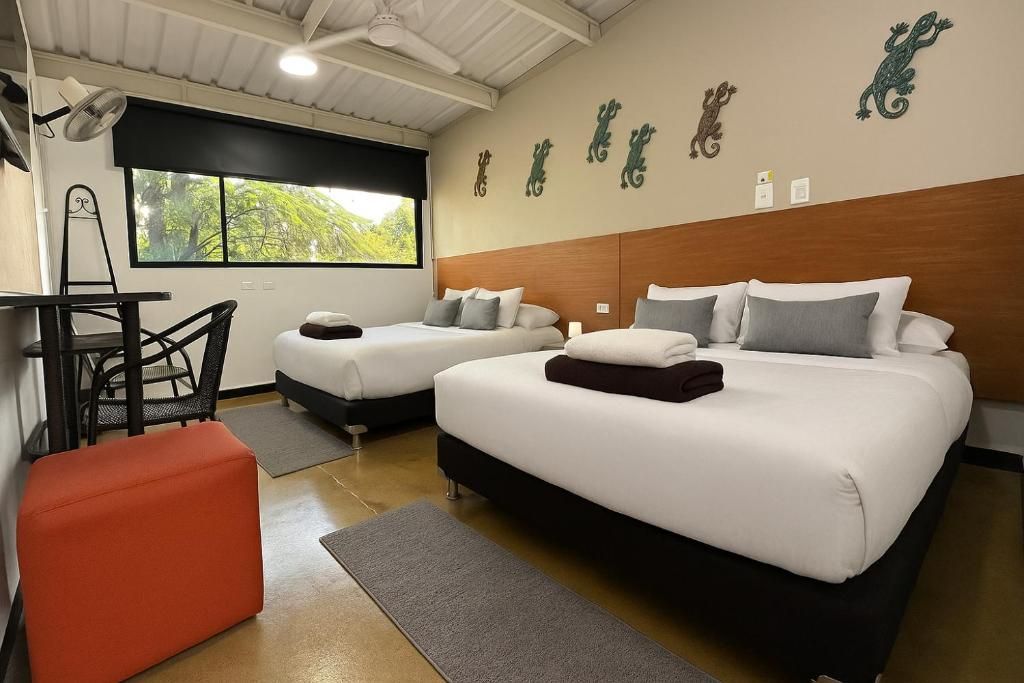 Habitación de hotel con dos camas, un escritorio, una silla y una ventana con vistas a árboles.