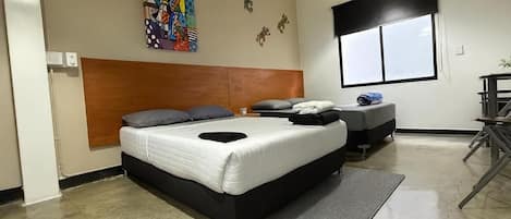 Habitación de hotel con una cama grande, una cama más pequeña, una ventana y una obra de arte colorida en la pared.