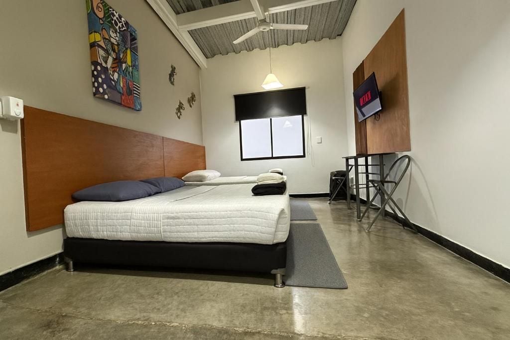 Een kamer met een bed, een plafondventilator, een raam en een aan de muur bevestigde televisie.