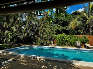Piscina com borda azulejada, rodeada por vegetação exuberante e cerca de madeira.