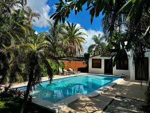 Piscina rodeada por vegetação exuberante e um edifício moderno com telhado inclinado.